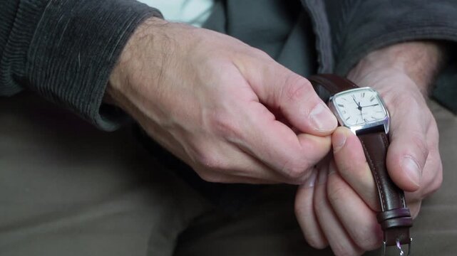 close up of a mans hand turning the crown of a classic silver wristwatch with a brown leather strap to set the time accurately symbolizing precision maintenance work and punctuality