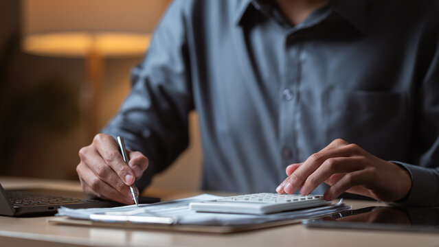 A person reviewing financial documents and using a calculator to manage monthly budgeting and expenses. Finance concept. Monthly finance planning. Financial lifestyle concept.