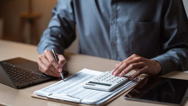 Close-up scene hands working on financial documents, using a calculator laptop to review data, manage budgeting tasks in office environment. Monthly finance planning. Financial lifestyle concept.