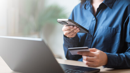 A person using a smartphone and credit card for secure online payment at a modern workspace. Using credit card payment. Online shopping purchase. E-commerce, E-business. Cashless contactless payment.