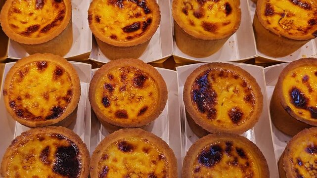 Fresh pastries and desserts at bakery display. Chocolate eclairs, cream tarts with macarons, and powdered sugar pastries arranged in boxes. Overhead view of sweet delicacies for sale.