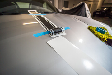 Installation of black foil stickers on the hood of a silver car. Detail of a vinyl sticker placed on the car during application.