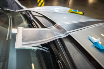 Installation of black foil stickers on the hood of a silver car. Detail of a vinyl sticker placed on the car during application.