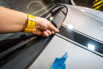 Worker installing car decals in garage, close-up of hand holding black vinyl film. Car decal application on hood.