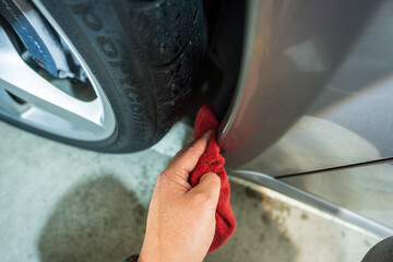 Close-up of a worker's hand washing the area around a car wheel with a red rag. Cleaning a car in a garage.