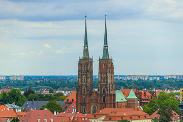 WrocÅaw cathedral with twin spires and red roofs against cloudy sky