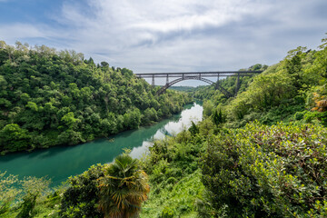 San Michele Bridge spans the Adda River with its elegant iron arch, one of the world&rsquo;s tallest single-span iron bridges, standing proudly amid lush hills and reflective waters.