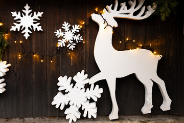 White styrofoam reindeer figure and snowflakes decorated with yellow string lights on dark wooden wall with fir branches.