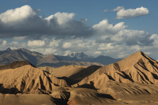 Arid hills and distant snow-capped peaks in Naryn Province, Kyrgyzstan, captured under partly cloudy skies.