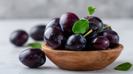 Fototapeta premium Fresh juicy plums in wooden bowl with leaves on light background