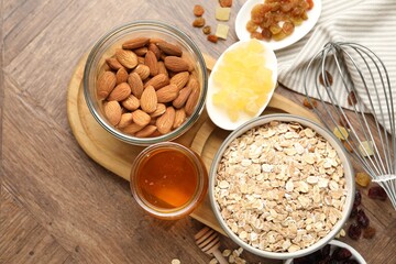 Making granola. Oat flakes in bowl, dried fruits, almond nuts and honey on wooden table, flat lay