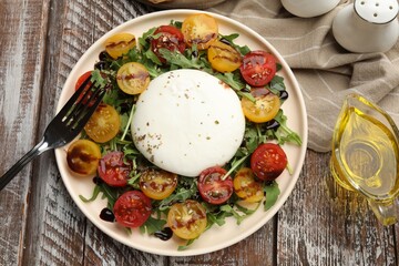 Delicious burrata cheese with arugula, tomatoes and dressing on wooden table, flat lay