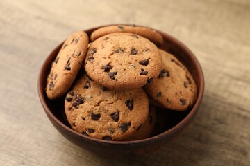 Delicious chocolate chip cookies in bowl on wooden table, closeup