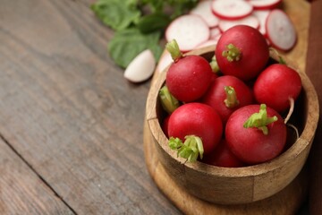 Fresh radishes in bowl on wooden table, closeup. Space for text