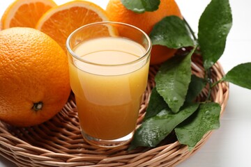 Fresh orange juice, fruits and leaves in basket on white table, closeup
