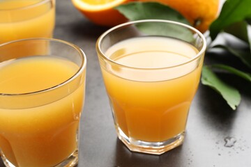 Fresh orange juice, fruits and leaves on grey table, closeup