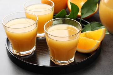 Fresh orange juice, fruits and leaves on grey table, closeup