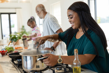 Diverse family cooking in home kitchen, stirring steel pot on gas cooktop and grating vegetables