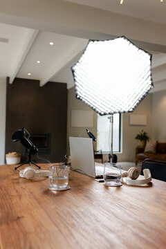 Condenser microphones are sitting on table with laptop, headphones and cables under softbox at home