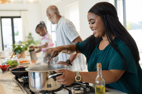 Diverse family cooking in home kitchen, stirring steel pot on gas cooktop and grating vegetables