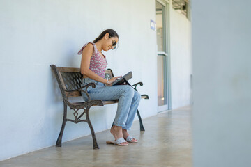 Latina woman using tablet on bench outdoors