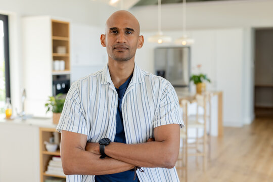Asian man standing with arms crossed at kitchen island with bar stools, pendant lights overhead