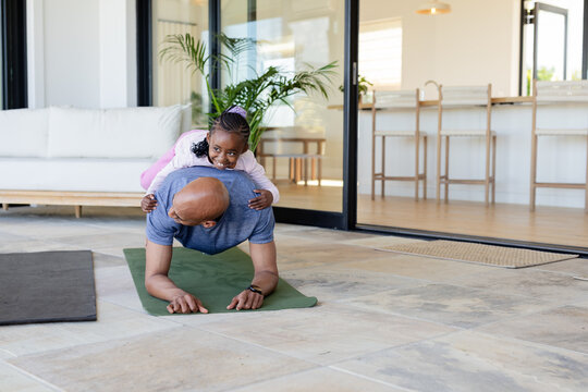African American father and daughter holding plank on green mat on patio beside sliding glass doors
