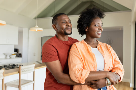Mid-adult African American couple embracing and gazing at counter in kitchen with pendant lights - Powered by Adobe