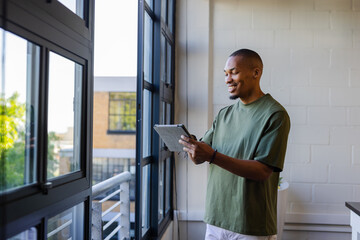 African American man standing in office interior with large windows holding tablet, copy space