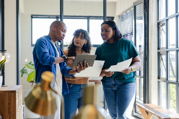 Diverse coworkers collaborating around digital tablet while reviewing documents in office space