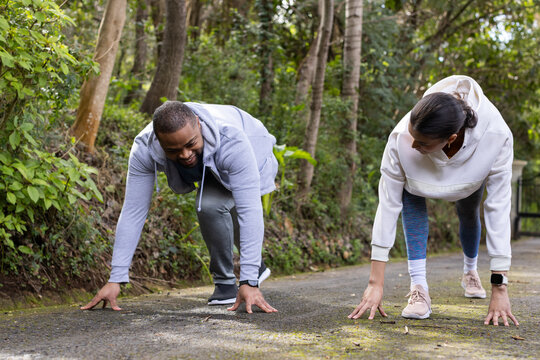 Diverse couple crouching and preparing to sprint on paved forest trail wearing athletic sneakers