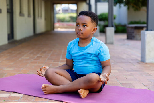 African American child sitting cross-legged meditating on purple mat on brick pavers in breezeway