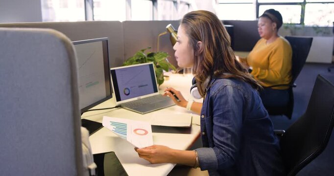 Reviewing bar charts mid adult woman annotating on laptop at office as coworker assisting colleague