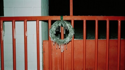 Dark Chirstmas Frozen wreath hanging on a red gate with icicles.