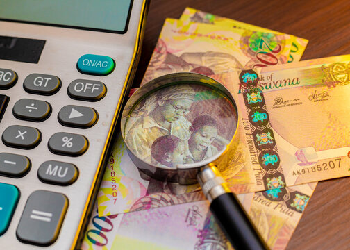 Botswana 200 Pula banknotes on a wooden desk with a magnifying glass and calculator. This professional composition represents financial auditing, education funding, and Botswana's local economy.