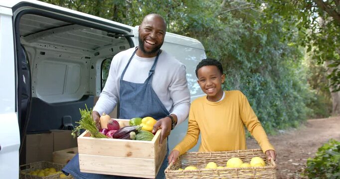 African American father and son stepping off van carrying vegetable crate and lemons on dirt lane