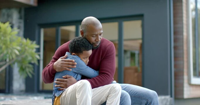 African American father and son on stone step, son climbing onto lap while father reassuring him