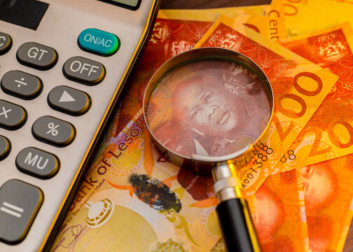 A magnifying glass focuses on a King Letsie III portrait on Lesotho 200 Maloti notes next to a calculator. This professional setup represents financial analysis, Southern African economy, and cash.