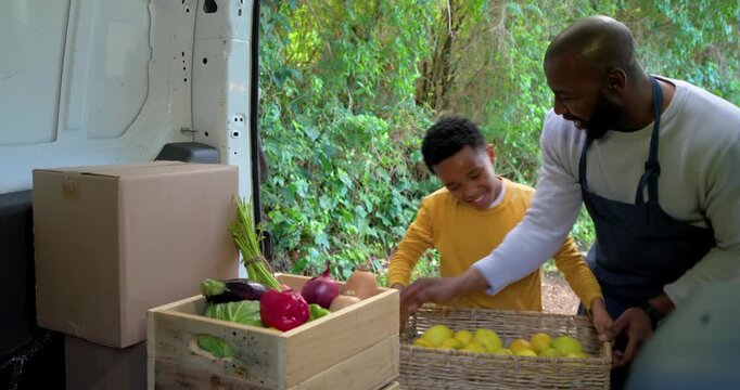 At van African American father dumping lemons showing onion guiding son placing pepper in crate