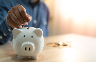 A man hand putting coins into a white piggy bank for account save money. Planning step up, saving...