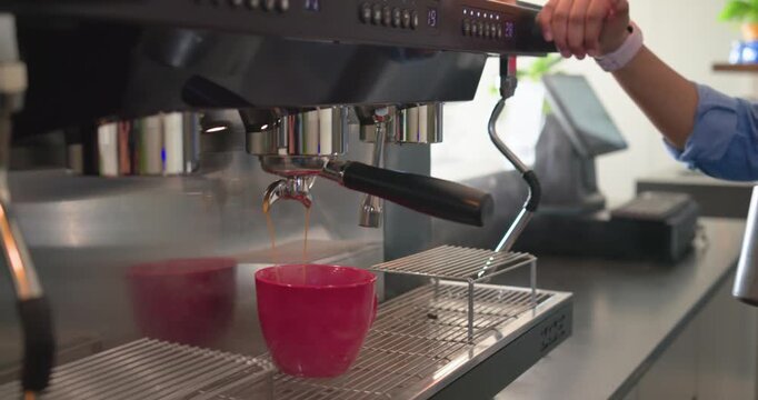 Female barista using espresso machine filling cup steaming milk for latte in cafe, copy space