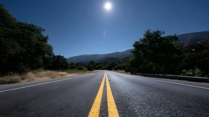 An empty asphalt highway stretches towards distant mountains under a bright sunny blue sky