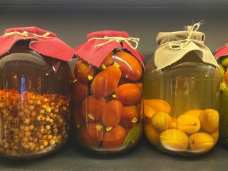 Homemade preserves in glass jars with fabric toppers and lids tied with twine. Pickled tomatoes, berries and apricots