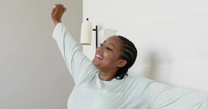 Mid adult African American woman waking up in bed, stretching arms over headboard feeling refreshed