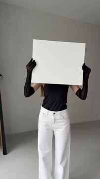 Woman holding a white square sign/poster in front of her body, facing the camera.