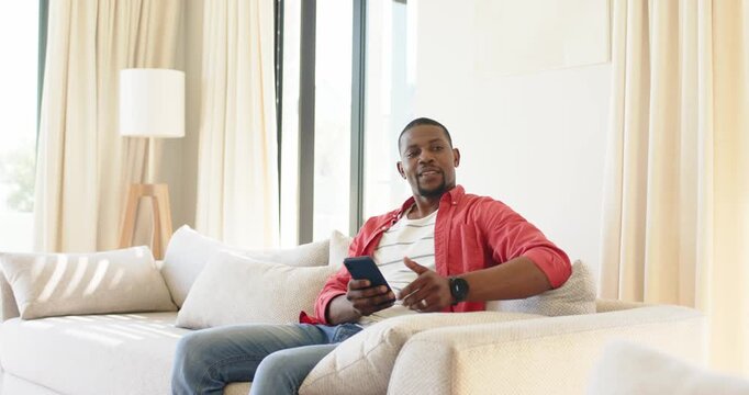 Mid-adult African American man scrolling smartphone at home raising thumb acknowledging friend