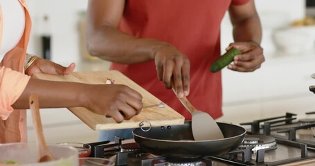 African American couple scraping shallots into pan and stirring spatula at stovetop to prepare meal