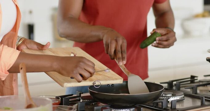 African American couple scraping shallots into pan and stirring spatula at stovetop to prepare meal