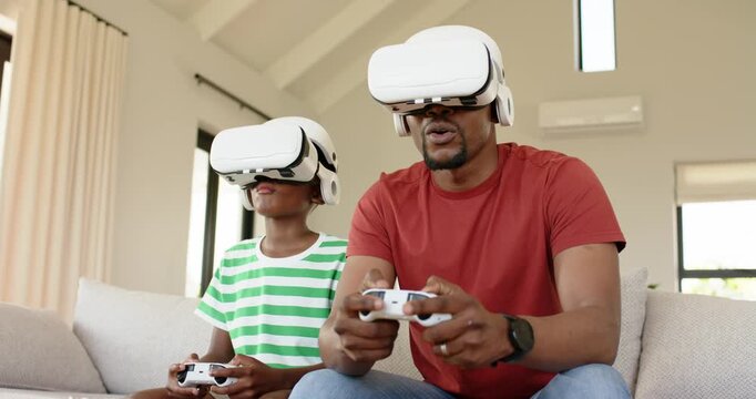 African American father and son grabbing VR headsets and controllers for gaming on living room sofa