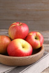 Ripe red apples in bowl on wooden table, closeup